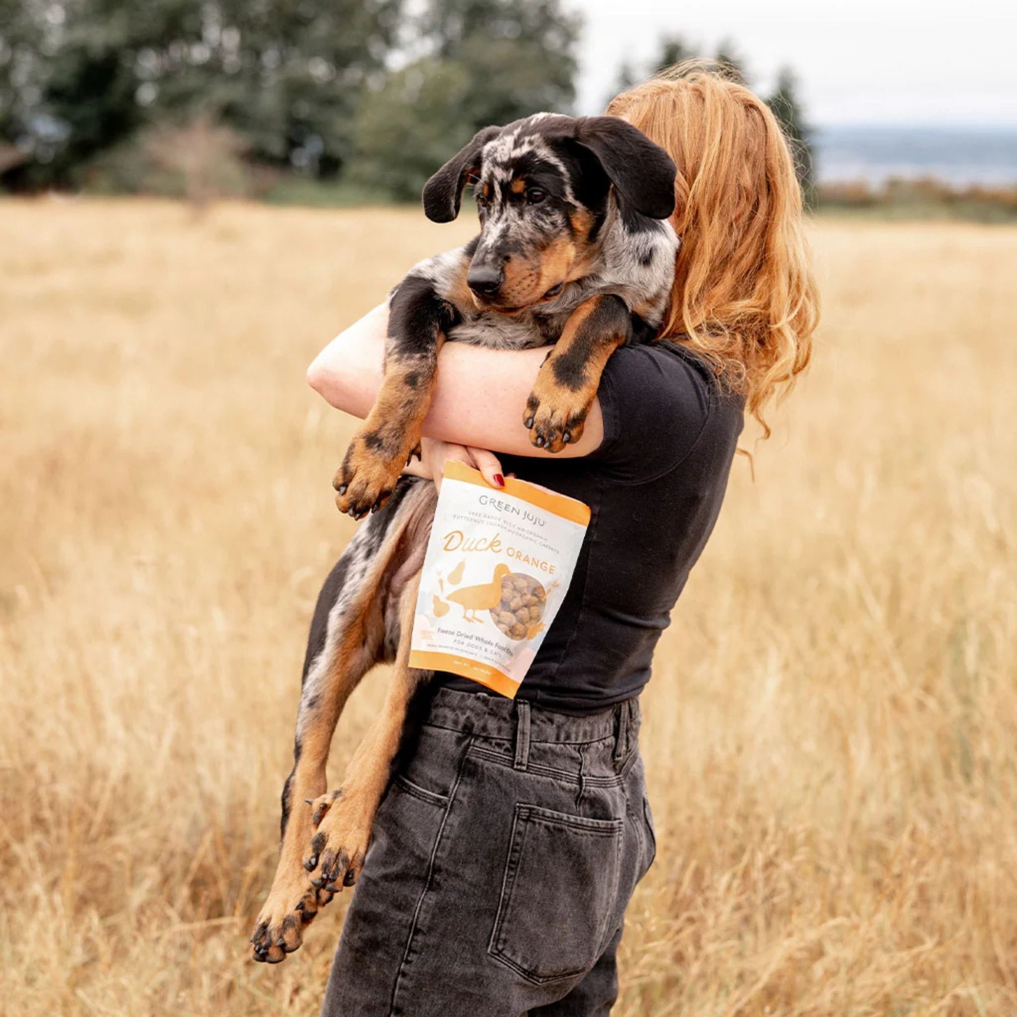 girl holding a dog and bag of green juju duck orange